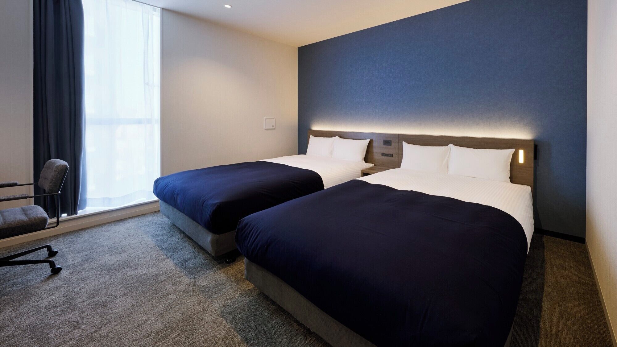 Ein Hotelzimmer mit zwei Betten, einem Schreibtisch und einem Stuhl.