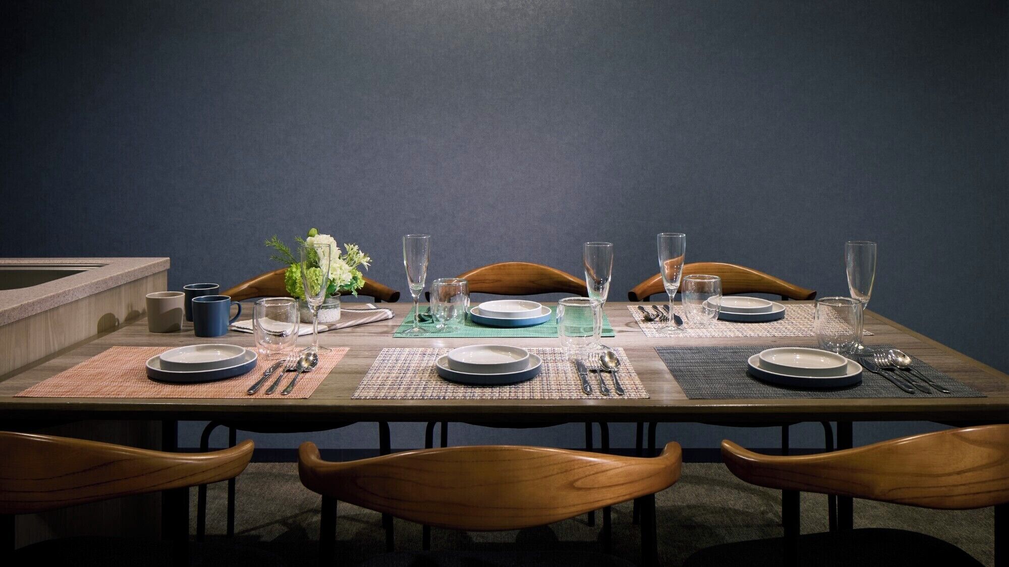 A dining table set with plates, glasses, and cutlery, surrounded by wooden chairs.