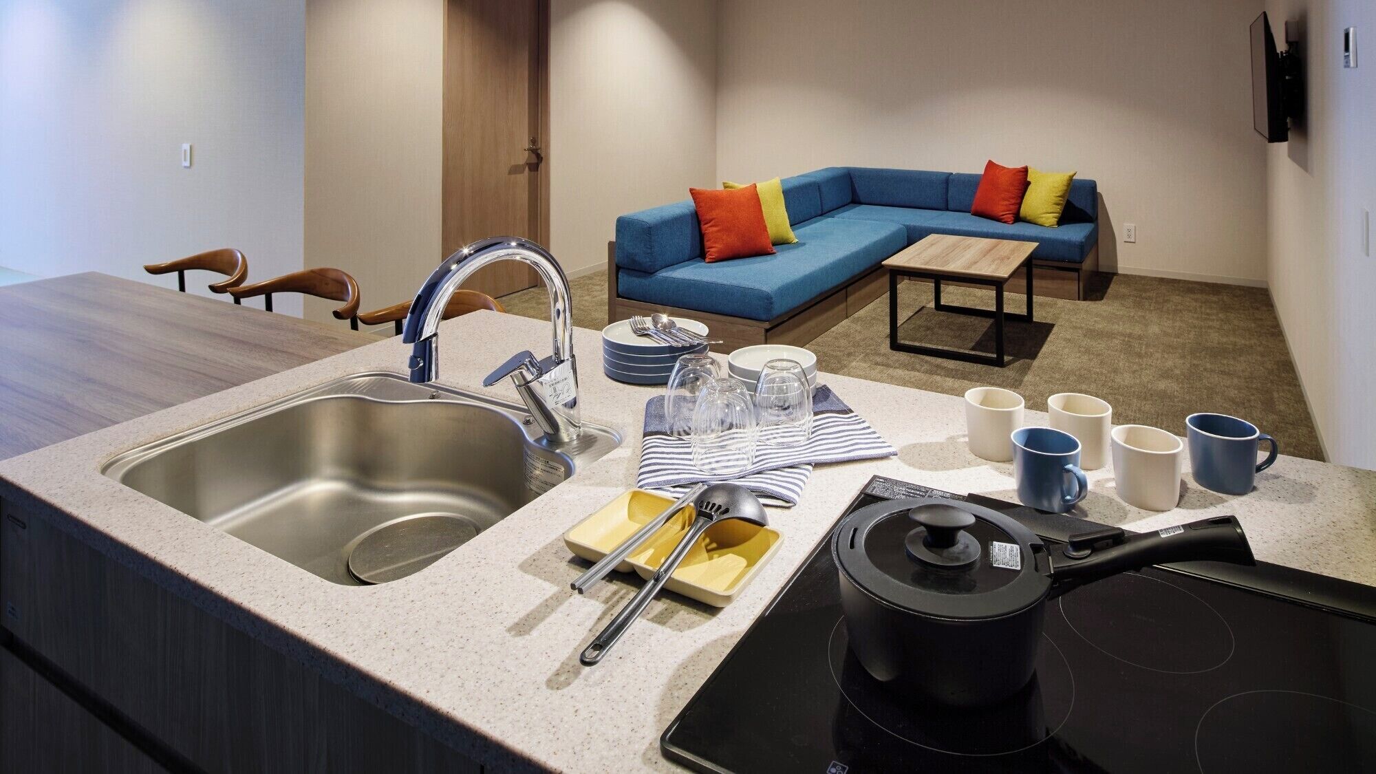 A modern kitchen with a double sink, a stove, and a dining area with a blue sofa and colorful cushions.