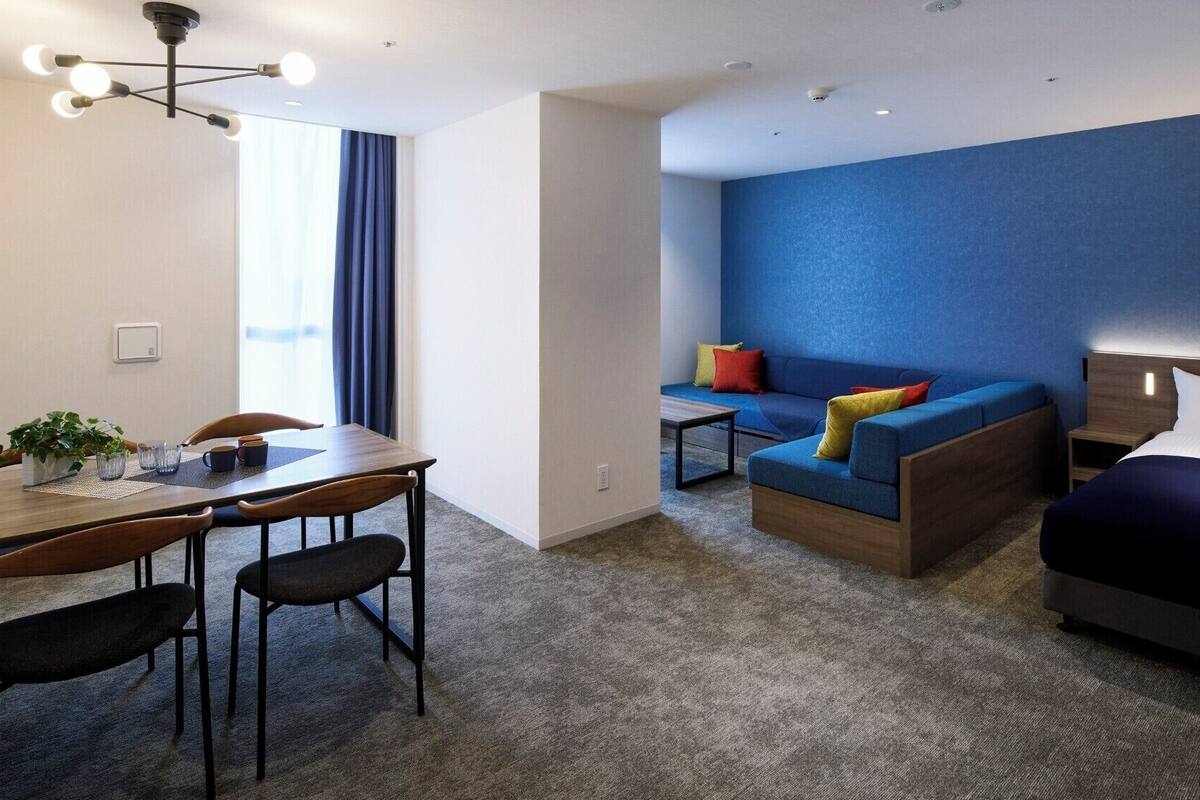 Quarto de hotel moderno com área de refeições, um conjunto de sofás e uma cama.