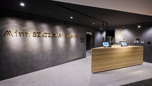 Una moderna recepción con detalles de madera, una pared oscura con el texto "Minr. Station Ai Nagoya" iluminado en dorado, y un diseño limpio y minimalista.