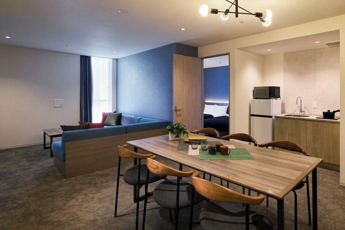 Um apartamento moderno com área de jantar, cozinha compacta e sala de estar com sofá e janela.