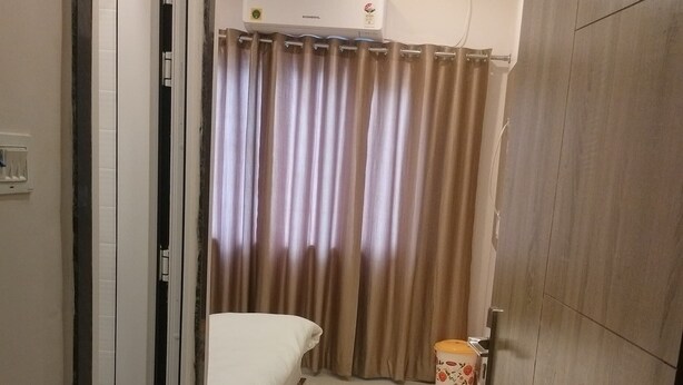 Una camera d'albergo con un letto, una porta, una tenda, un cestino e un piccolo tappetino.
