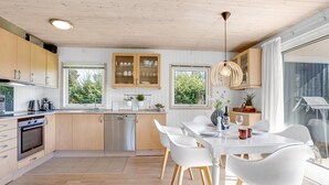 Eine moderne Küche mit Holzschränken, einem Geschirrspüler und einem Essbereich mit weißen Stühlen und einem Tisch.