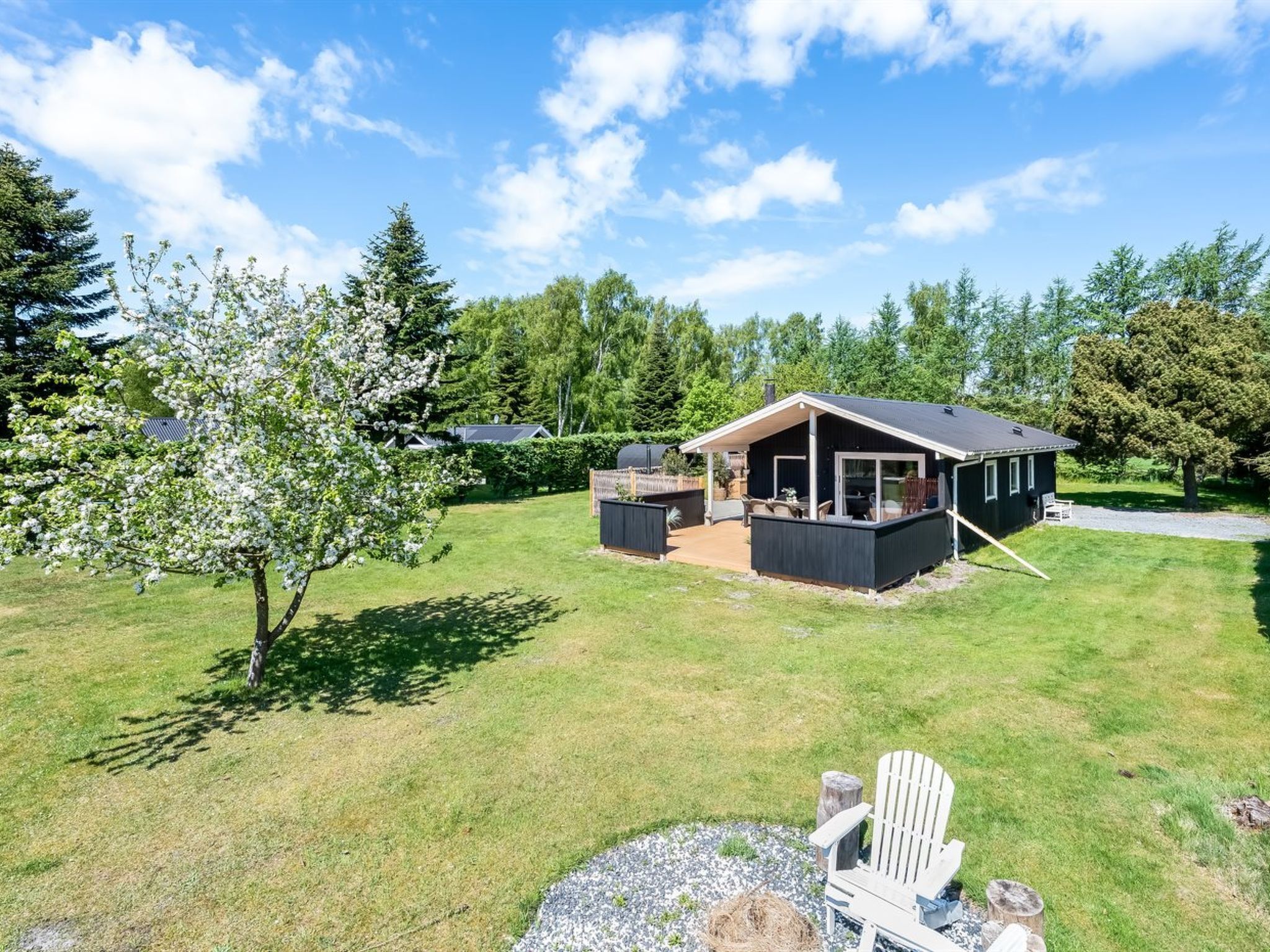Une maison moderne dotée d’un patio couvert, d’une pelouse et d’un arbre aux fleurs blanches.