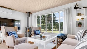 Ein gemütliches Wohnzimmer mit Kamin, bequemen Sitzgelegenheiten und einem großen Fenster mit Blick ins Freie.