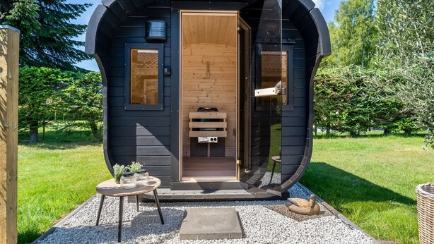 Eine kleine, dunkle Holzhütte mit kreisförmigem Design, einer Holztür und einem kleinen Tisch mit Gläsern.