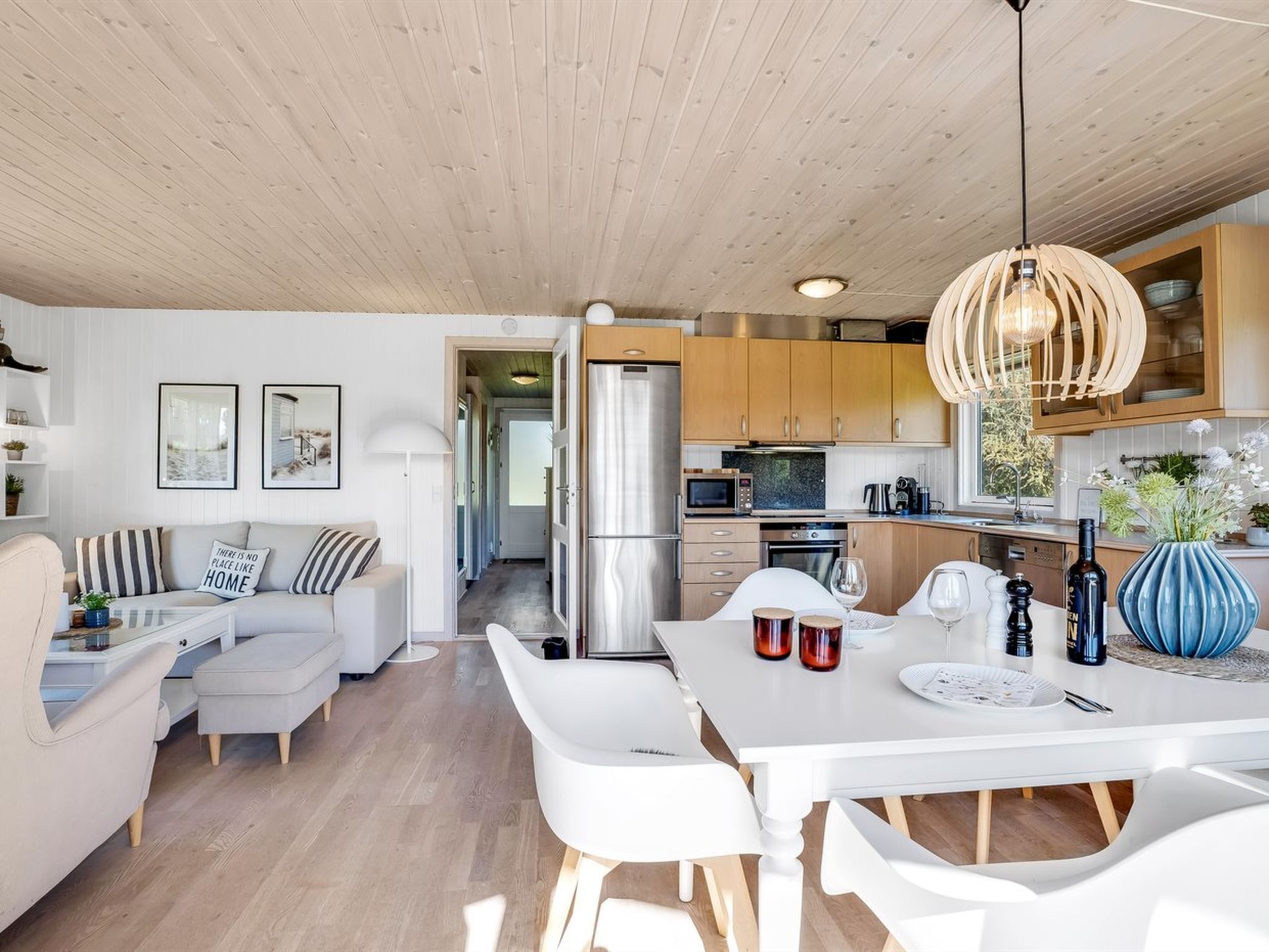 Eine moderne Küche mit Holzschränken, einem Edelstahlkühlschrank und einem Essbereich mit weißem Tisch und Stühlen.
