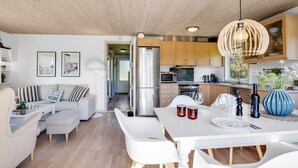 Eine moderne Küche mit Holzschränken, einem Edelstahlkühlschrank und einem Essbereich mit weißem Tisch und Stühlen.