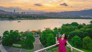A woman in a pink dress standing on a balcony with a cityscape and river in the background. - the Star Hotel (Zhaoqing)
