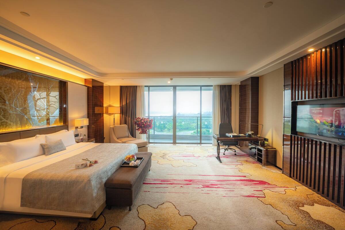A modern hotel room with a large bed, a sofa, a desk, and a TV.