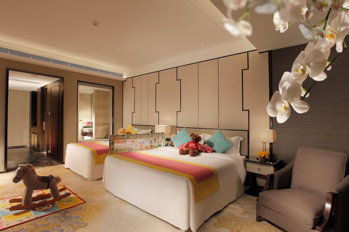 A hotel room with two beds, a rocking horse, a nightstand with a lamp, and a chair.