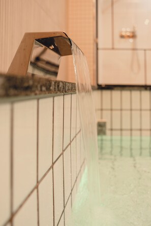 Ein Badezimmer mit gefliesten Wänden und einem Waschbecken mit fließendem Wasser.