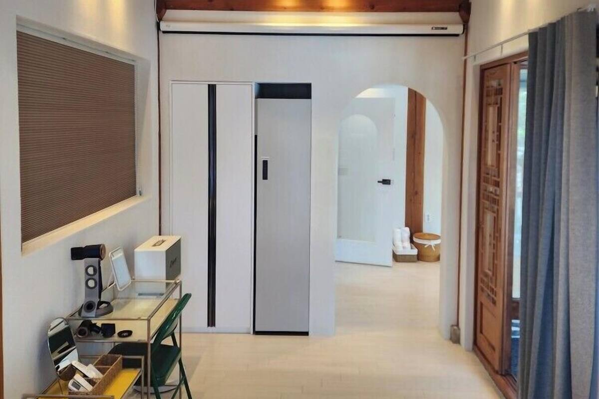 A modern hotel room with a wooden ceiling, a desk with a computer, a bed, and a bathroom visible through an open door.