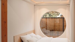 Une chambre avec une fenêtre circulaire, des poutres en bois, un lit et une petite table ronde.