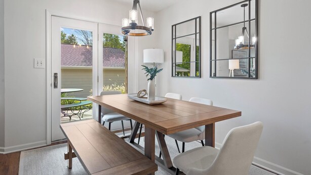 A dining area with a wooden table, white chairs, a bench, and a chandelier. There are two wall-mounted mirrors and a potted plant on the table. - 1.5  Miles to Mizzou! ~ Spacious & Updated Home~ (Columbia)