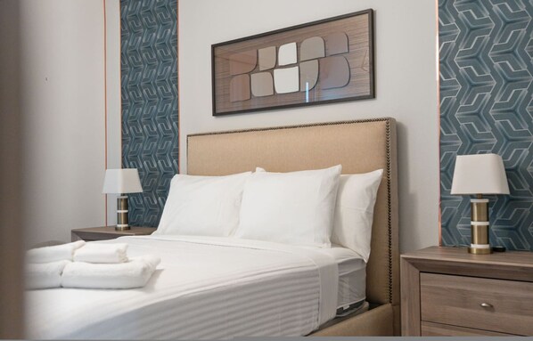 A neatly made bed with white linens, two bedside lamps, and a framed abstract artwork above the headboard. - Peaceful 3BR Oasis Private Pool -17522 (Clermont)