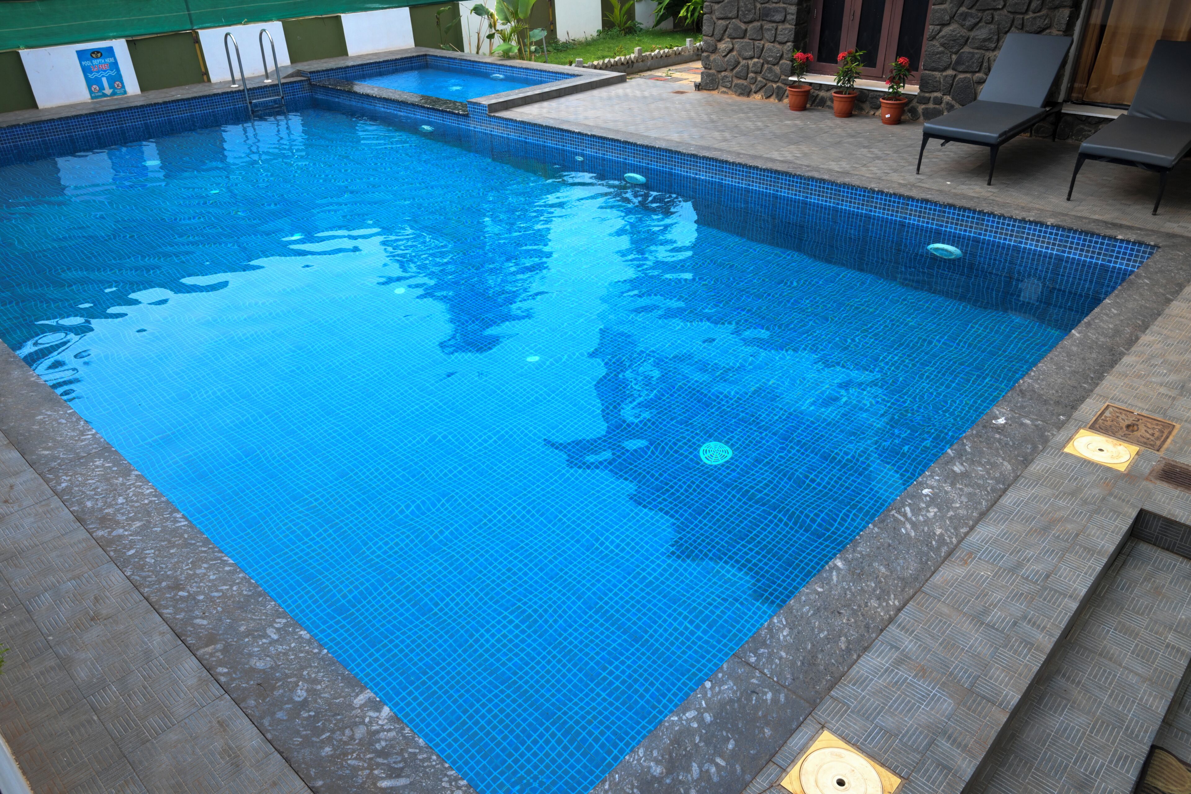 A rectangular pool with a tiled edge, a stone wall, and a small seating area with potted plants.