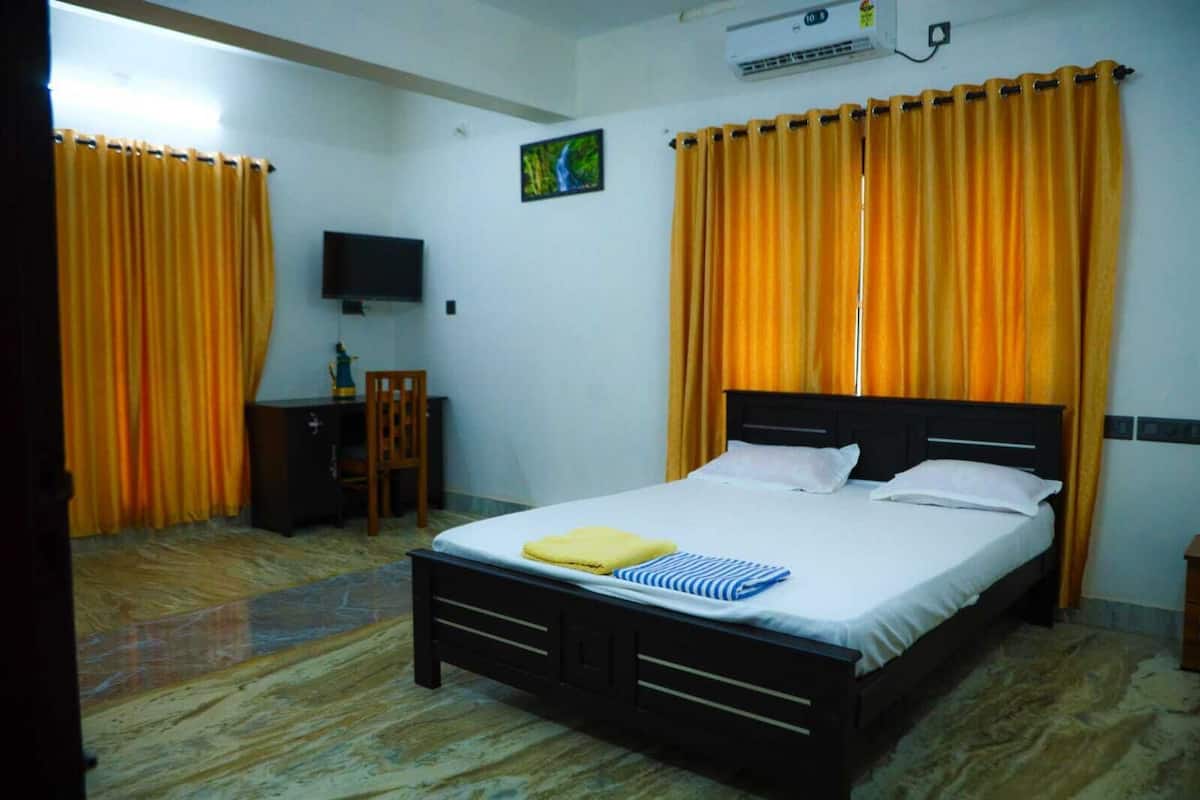 A bedroom with a bed, curtains, a desk, a chair, a television, and an air conditioning unit.