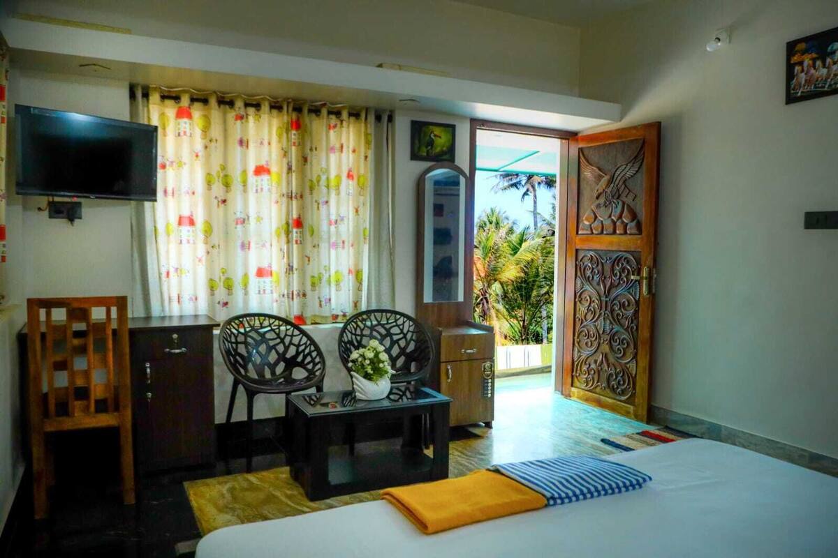 A hotel room with a bed, two chairs, a small table with a vase, a TV, and a decorative door.