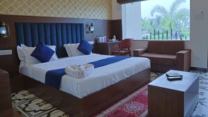 A hotel room with a large bed, a desk, a chair, and a window with a view of palm trees. - VITS Select Diamond Resort Sasan Gir  (Talala)