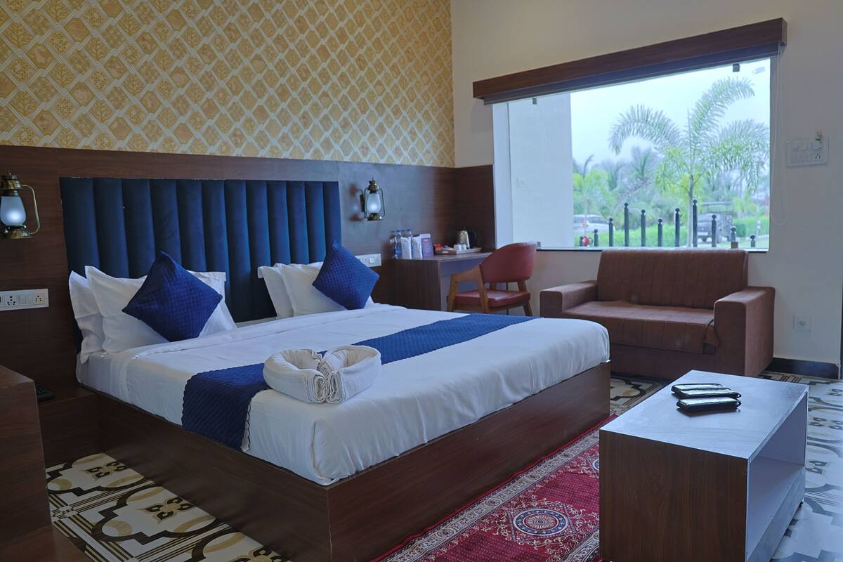 Habitación de hotel con una cama grande, un escritorio, una silla y una ventana con vista a palmeras.