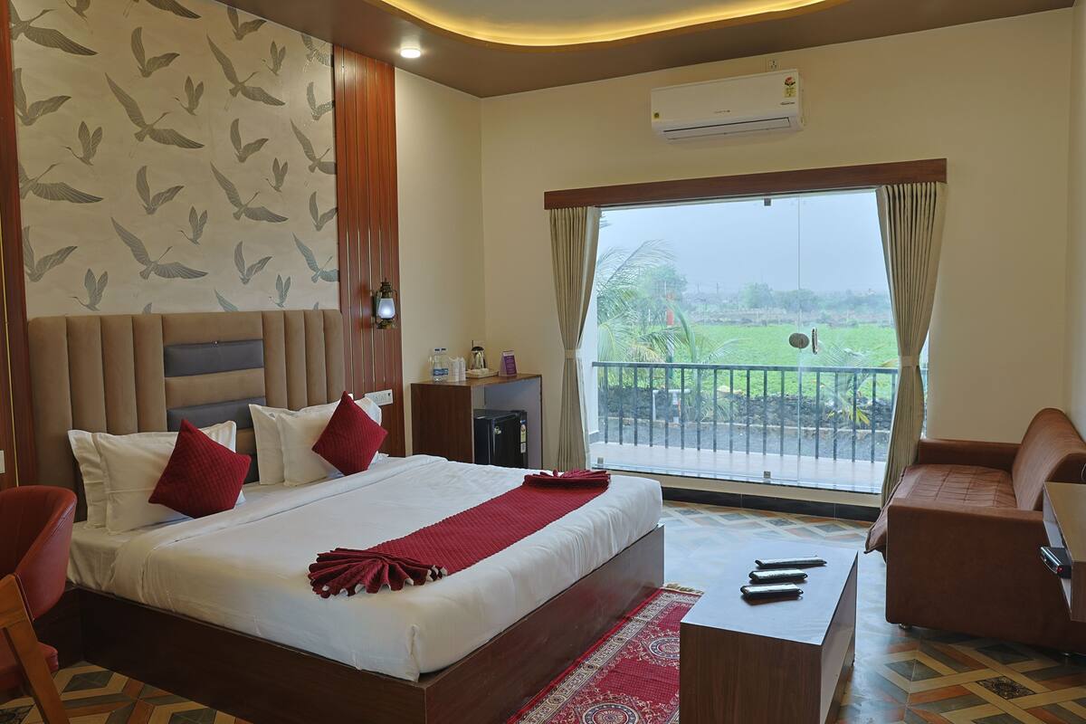 Habitación de hotel con una cama grande, un sofá, un escritorio y un balcón con vistas a zonas verdes.