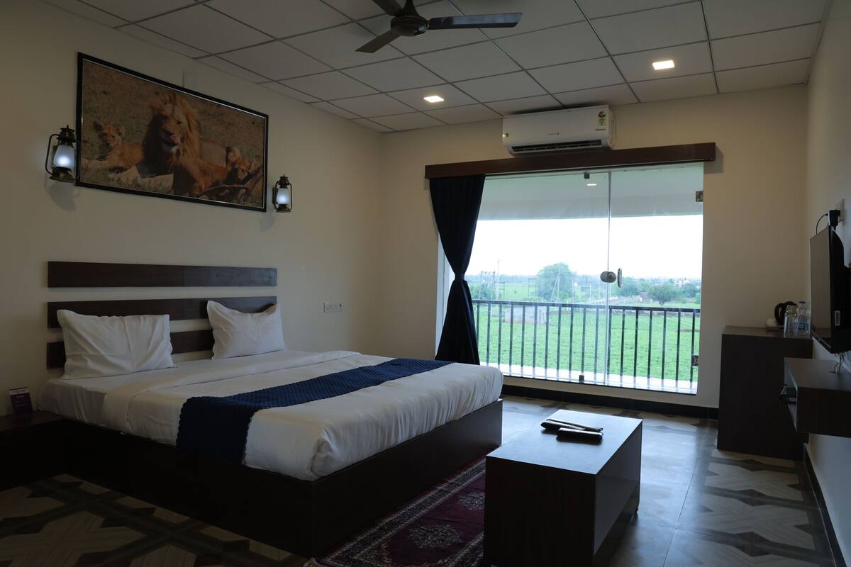 Habitación de hotel con una cama grande, ventilador de techo, televisor montado y balcón con vistas al exterior.