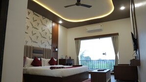 A hotel room with a bed, a desk, a ceiling fan, an air conditioner, and a view of the outdoors. - VITS Select Diamond Resort Sasan Gir  (Talala)