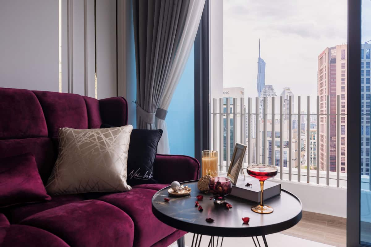 A modern living room with a red sofa, a small round table with a drink, and a city view through large windows.
