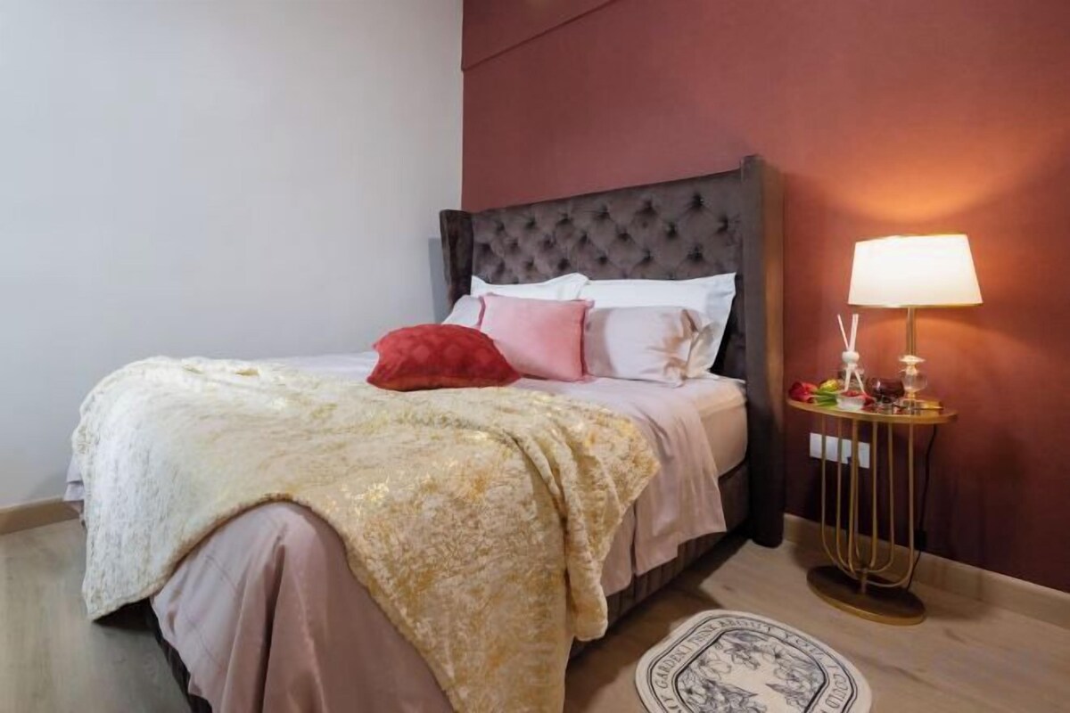 A bed with a headboard, pillows, a blanket, and a bedside table with a lamp.