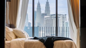 Une chambre d’hôtel avec un lit, des rideaux et une vue sur les tours Petronas.