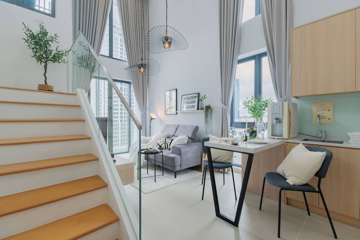 A modern apartment with a staircase, a living area with a sofa and dining table, and a kitchen with wooden cabinets.