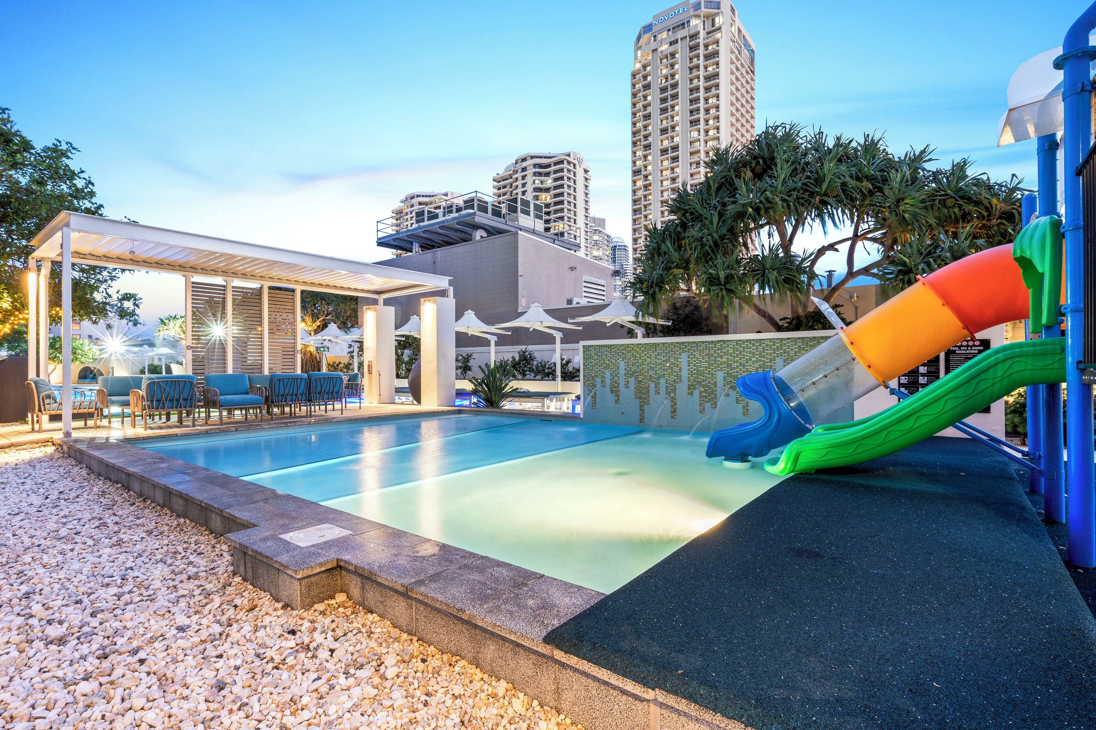 Una piscina con tobogán, sillas de descanso y una zona de estar cubierta.