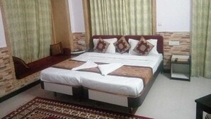 A bedroom with a large bed, a small bedside table, a wall-mounted air conditioner, and a window with curtains. - Hotel Regal Heritage Jaisalmer (Jaisalmer)