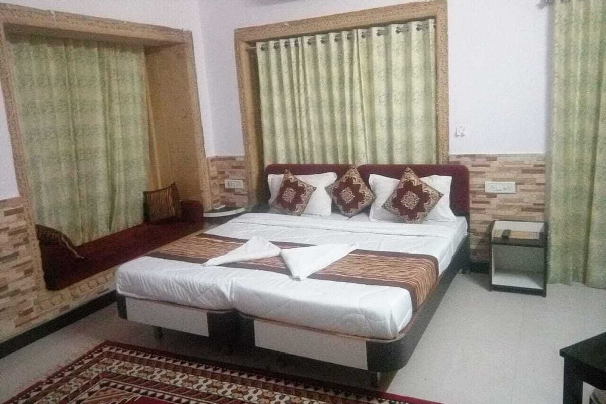 Ein Schlafzimmer mit einem großen Bett, einem kleinen Nachttisch, einer Wand-Klimaanlage und einem Fenster mit Vorhängen.