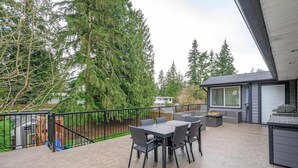Eine Terrasse mit Tisch und Stühlen, umgeben von einem Metallgeländer, mit Blick auf ein bewaldetes Gebiet.