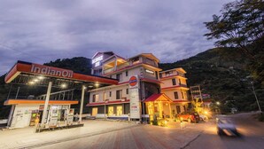 Un hotel de varios pisos con un llamativo rótulo de IndianOil, una gasolinera y una carretera con un vehículo en movimiento.