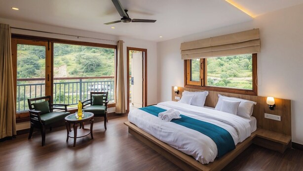 Habitación de hotel con una cama grande, ventilador de techo, balcón con una silla y mesa, y vista a zonas verdes.