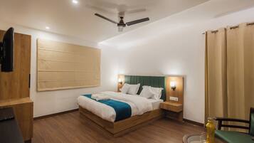A hotel room with a wooden bed, a ceiling fan, a bedside table, a chair, and a glass table with a bottle.