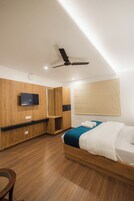 Habitación de hotel moderna con cama, armario de madera, ventilador de techo y televisor montado.
