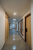 Un largo pasillo bien iluminado con puertas y ventanas de madera a ambos lados, que conduce a un extremo distante.