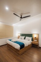 Una habitación de hotel moderna con una cama de madera, un ventilador de techo y un cabecero verde.