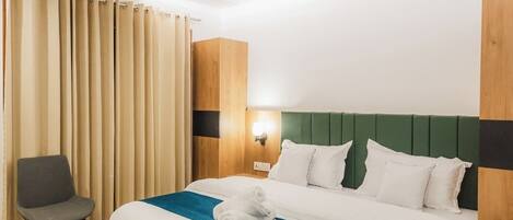 Habitación de hotel con cama de madera, cabecera verde, ventilador de techo, una silla y ventana con cortinas.