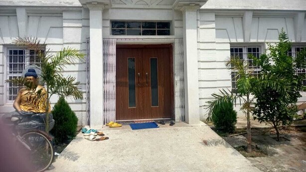 A building with a large arched entrance, a wooden door, and a small porch area with a bicycle and some items on the ground. - Hotel Bodhgaya Inn By GRB (Gaya)