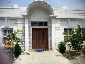 A building with a large arched entrance, a wooden door, and a small porch area with a bicycle and some items on the ground. - Hotel Bodhgaya Inn By GRB (Gaya)