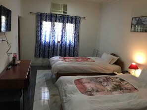 A hotel room with two beds, a desk, a chair, a lamp, and a painting on the wall.