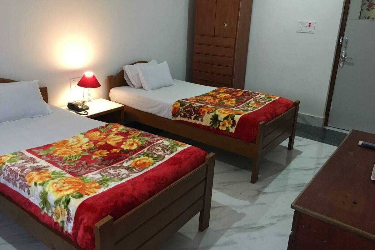 A hotel room with two single beds, a wooden wardrobe, a desk, and a nightstand with a lamp.