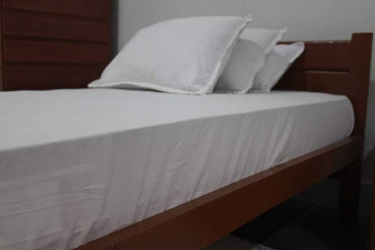 A single bed with white bedding and a wooden headboard in a room with a plain wall.