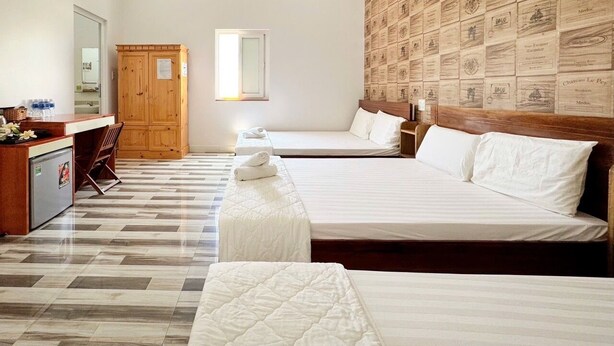 A hotel room with two beds, a wooden wardrobe, a desk with a chair, and a tiled floor. - Chan Hotel Phu Quy (Phu Quy)